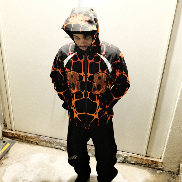 Person wearing a black and orange patterned jacket standing in front of a white door.