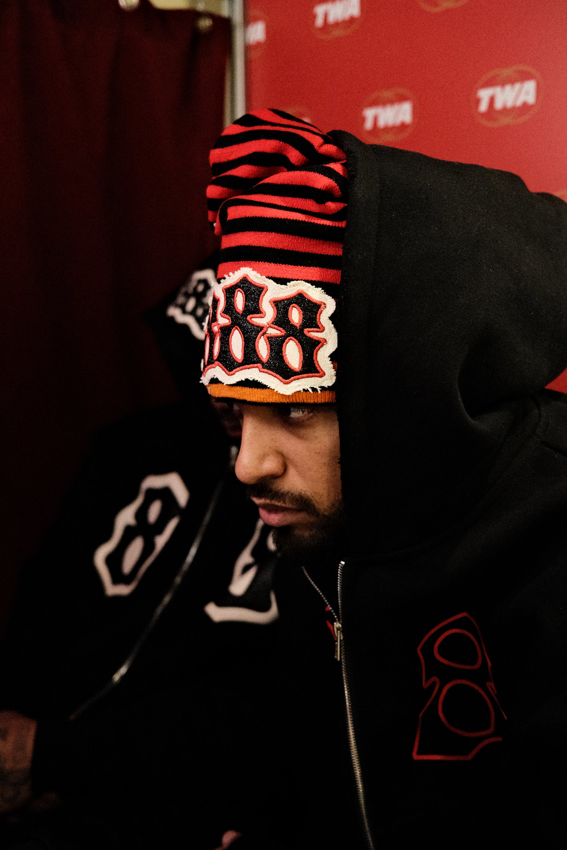 Person wearing a black hoodie with red and white designs on a red background