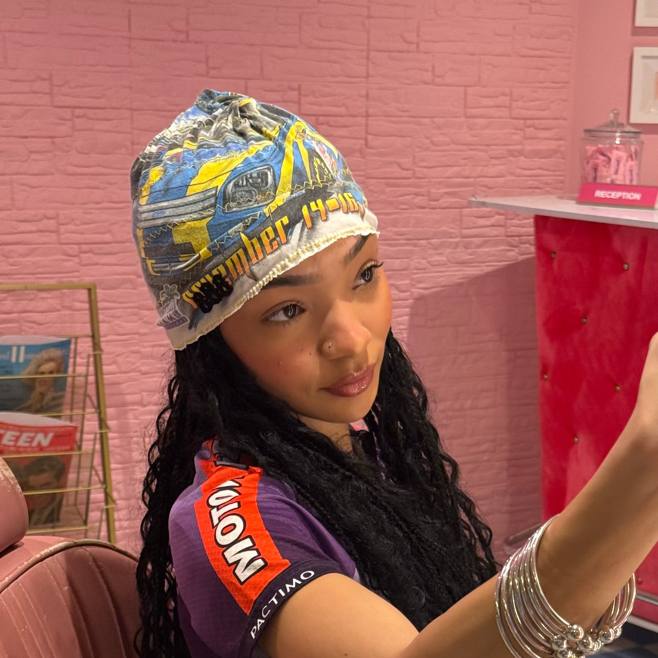 Person taking a selfie in a salon chair with a pink wall and vintage decor.
