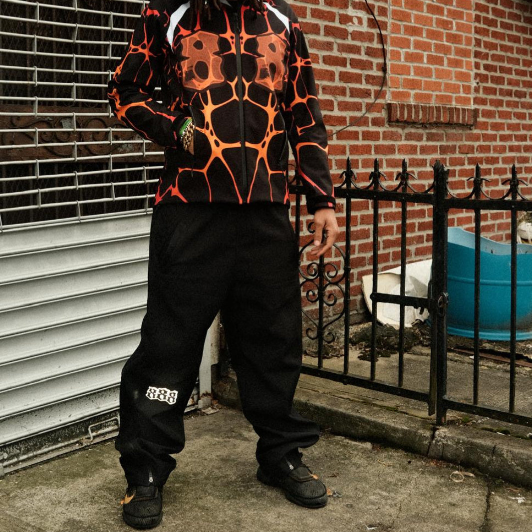 Person wearing a black and orange hoodie standing on a sidewalk with a brick building in the background.