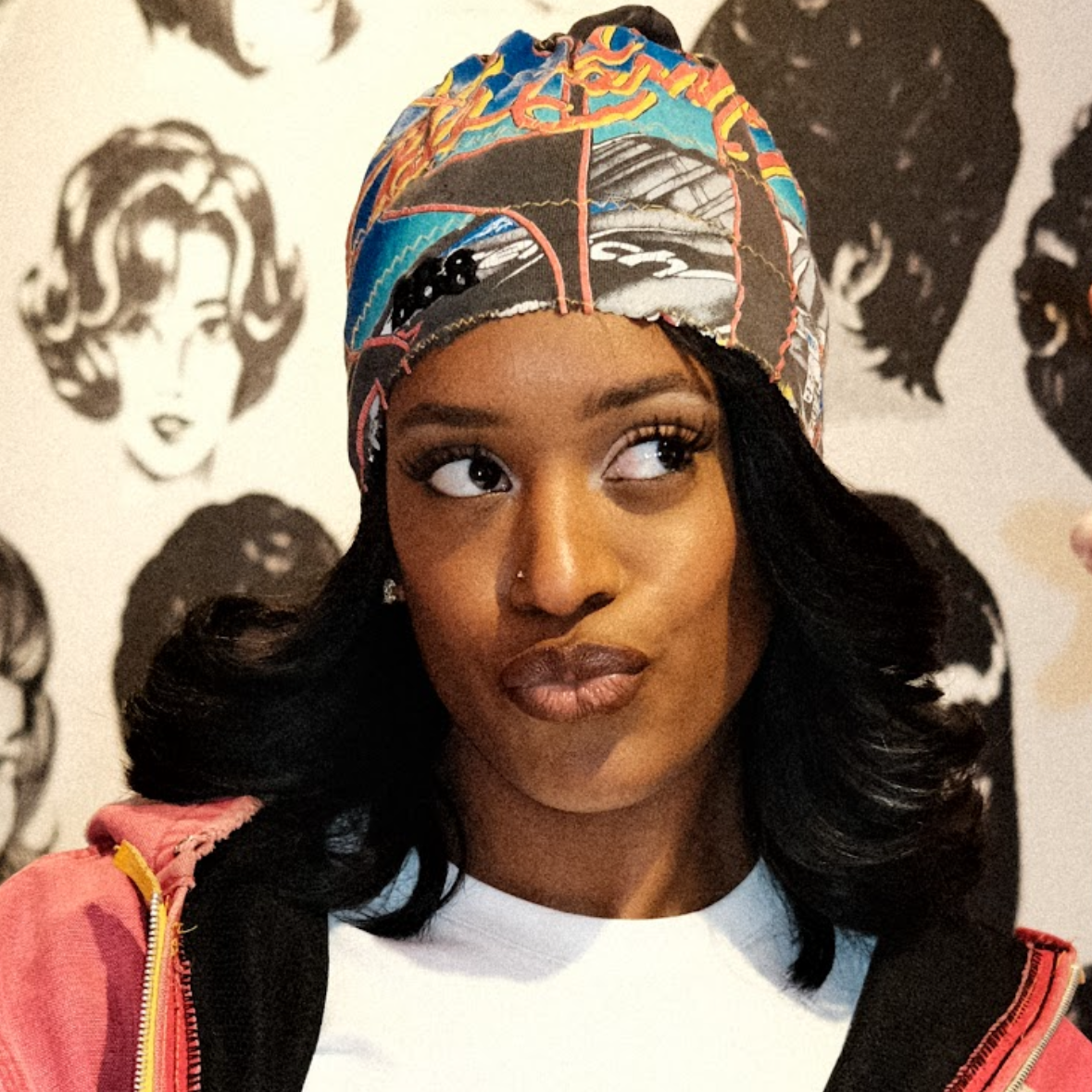 Woman wearing a colorful headscarf with a patterned background featuring hair styles.